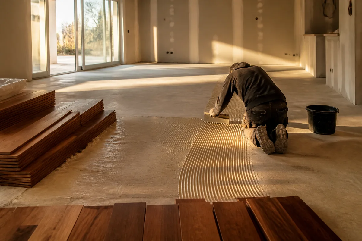 Poseur encollant une chape au peigne cranté avant la mise en place d&rsquo;un parquet massif exotique